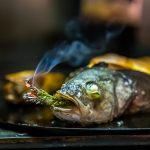 Der Loup de Mediterranée gefüllt mit einem zart getrüffelten Souffle von Cyril Aveline räuchert sich noch im Jospergrill selbst mit einem Rosmarinzweig / © Foto: Georg Berg