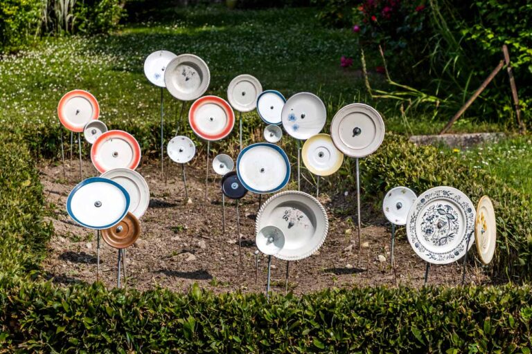 Placas en postes en un jardín delantero en Francia, Nouvelle-Aqutaine. El motivo coincide con el proverbio alemán "Über den Tellerrand schauen" (piensa fuera de la caja) y hace referencia a una actitud abierta y curiosa en la que uno está dispuesto a cruzar sus propios límites y aprender cosas nuevas. La frase se utiliza a menudo en relación con el cosmopolitismo, el cambio de perspectiva o la innovación / © Foto: Georg Berg