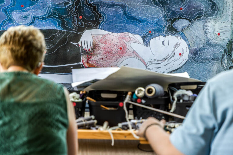 Cartonage mit einem Ausschnitt aus dem Motiv des Teppichs "Hommage à George Sand" von Francoise Petrovitch. Die Künstlerin legt besonderen Wert auf harmonische Übergänge, fragmentierte Farbfelder und subtile Düsterkeit. Die Tapisserie verbindet kräftige und zarte Farbbereiche, um poetische, aber dennoch gesellschaftskritische Bildwelten zu erzeugen. Die Webtechnik und Farbumsetzung erfolgen in enger Zusammenarbeit mit den lokalen Färberinnen und Weberinnen, um die gewünschte Nuancierung und Tiefenwirkung der Tuschezeichnungen der Künstlerin in textile Form zu übersetzen / © Foto: Georg Berg