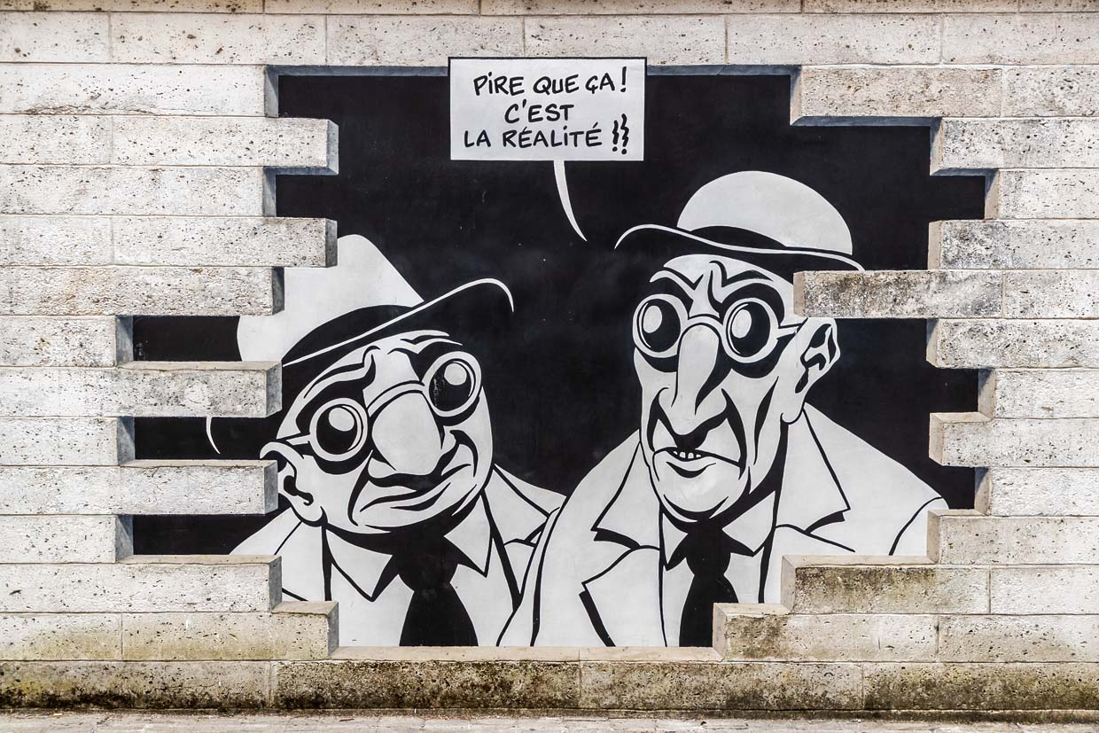 Wandgemälde aus der Serie „Réalité, Sortie de Secours” (Realität, Notausgang), die von Marc-Antoine Mathieu entworfen wurde. Es zeigt Comicfiguren mit Sprechblasen, die aus der Wand hervorzubrechen scheinen. "Sehen Sie etwas?" "Ja, schauen Sie. Es ist genau das, was ich befürchtet habe." "Was, schon wieder eine Unterwelt?" "Schlimmer als das. Es ist die Realität.". / © Foto: Georg Berg